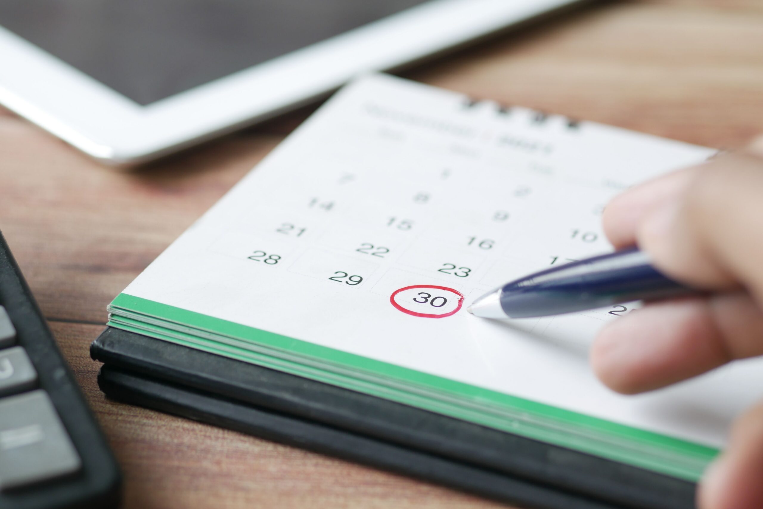 A person holding black pen pointing on calendar